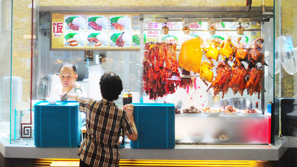 A male hawker interacts with a woman standing at a food stall counter in Singapore. joyfull/Shutterstock